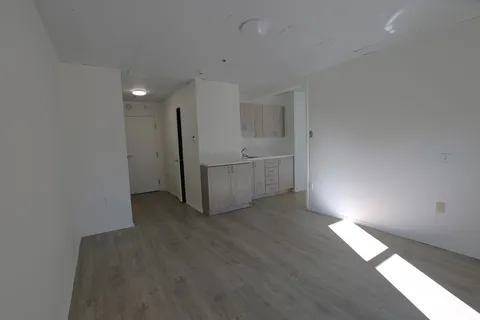 Empty room with pale flooring and a compact white kitchenette.