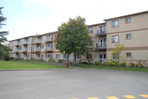 Residence wing with balconies beside a paved parking area.