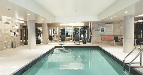 Indoor pool with handrails, deck seating and surrounding windows.