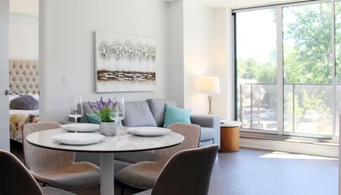 Suite dining and living area with a table, sofa and balcony doors.