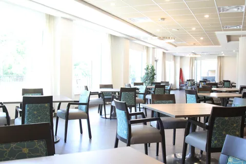 Dining area with tables, upholstered chairs and large windows.
