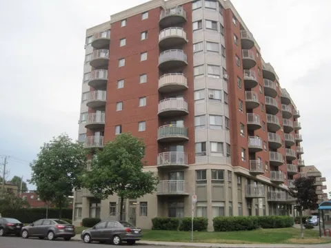Brick residence with curved balconies, trees, shrubs and parked cars