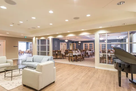 Seating area with a sofa, armchairs and a grand piano beside an open dining room
