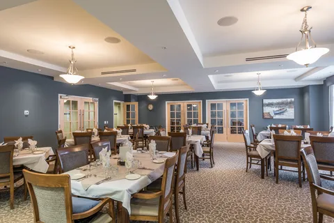 Dining room with set tables, wooden chairs, glass doors and a painting of a boat