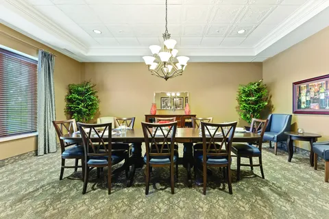 Dining table beneath a chandelier with chairs and potted trees