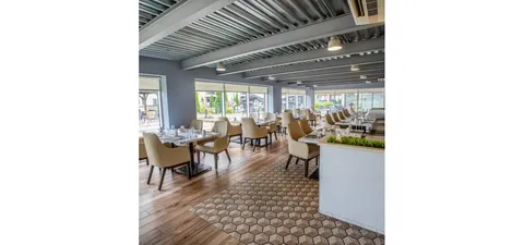 Dining room with set tables and upholstered chairs beside windows.