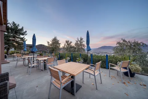 Outdoor terrace with tables, chairs and closed parasols at sunset.