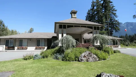 Low residence building with a covered entrance, flower beds and mountains behind