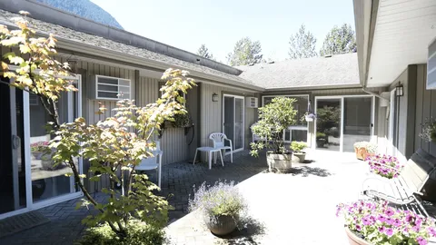 Paved courtyard with chairs, a bench, potted trees and flowers