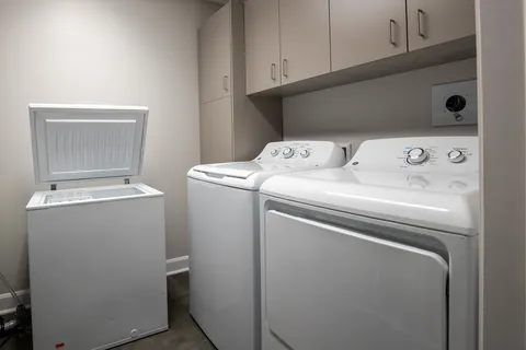 Laundry closet with a washer, dryer, cabinets and a small chest freezer.