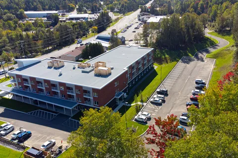 Aerial rear view of the brick residence, balconies, parking spaces and surrounding trees.