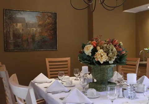 Round dining table set with glasses and napkins beneath a framed landscape
