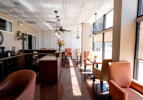 Counter and tables with orange chairs beside tall windows