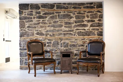 Two chairs beside an exposed stone wall.