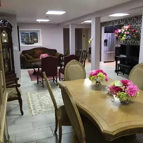 Dining table with flowers and upholstered chairs beside a sitting area and piano