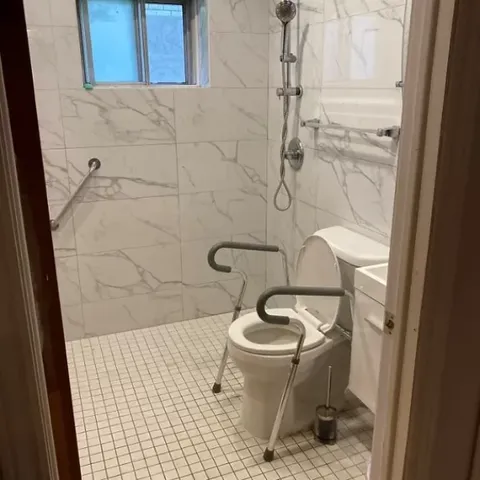 Bathroom with a tiled shower, toilet, grab rails and a window
