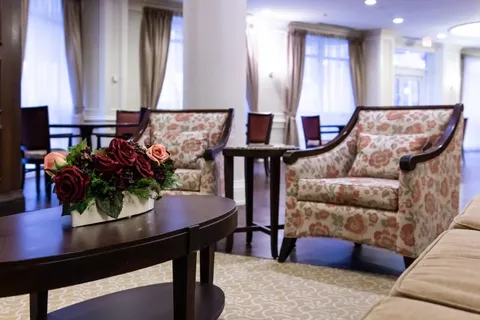 Two armchairs and a flower-topped table beside large windows