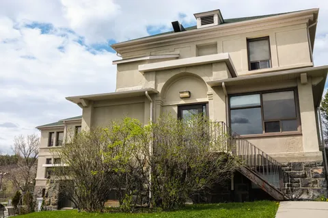Side of a cream building with windows, shrubs and an outdoor staircase