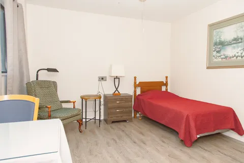 Bedroom with a red bedspread, bedside cabinet, lamp and green armchair