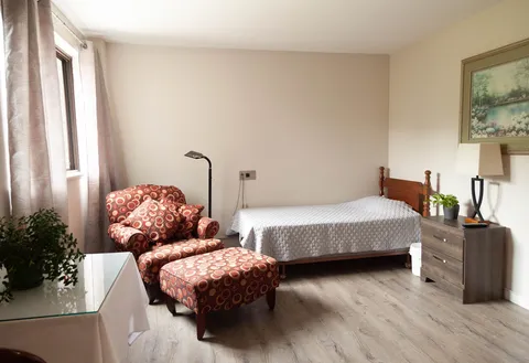 Bedroom with a single bed, patterned armchair, footstool and bedside table