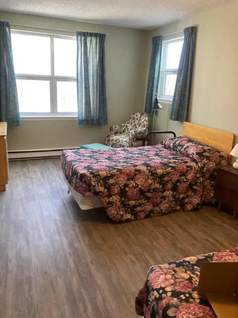 Bedroom with a floral bedspread, an armchair and two windows