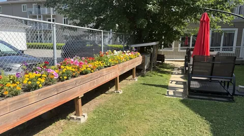 Raised flower beds beside lawn chairs and a red patio umbrella.