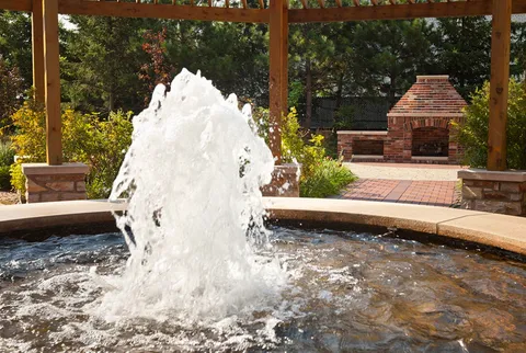Fountain beneath a wooden pergola beside an outdoor fireplace