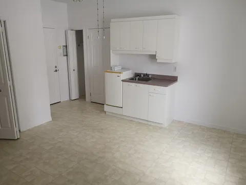 Unfurnished room with white kitchenette cabinets, a sink and tiled flooring