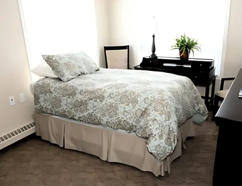Bedroom with patterned bedding, dark drawers and an armchair
