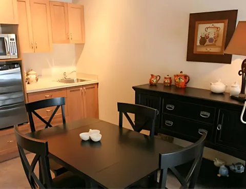 Dining table and chairs beside wooden kitchenette cupboards and a sideboard