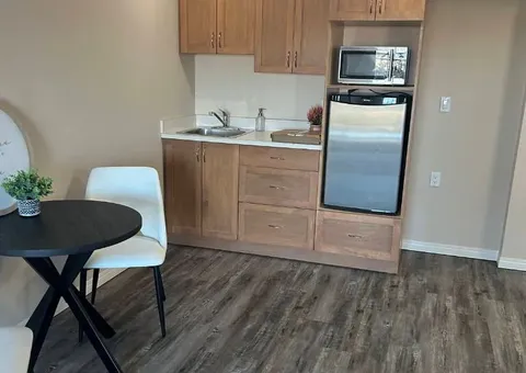 Wooden kitchenette cupboards, sink and appliances beside a small table