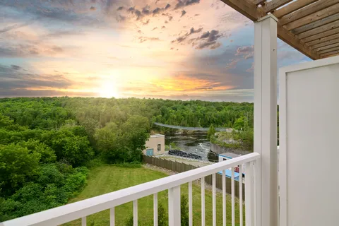 Balcony railing overlooking trees and a river at sunset
