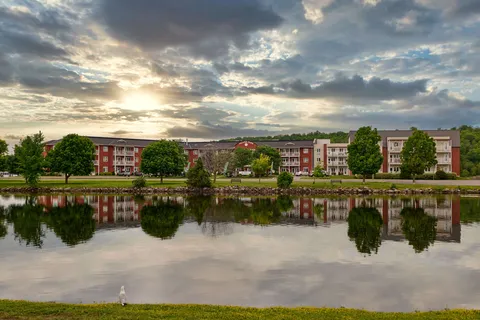 Three-storey residence across a river, with trees and the building reflected in the water