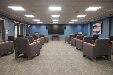 Room with rows of armchairs facing a blank television on a blue wall