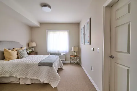 Bedroom with a bed, gold cushions, bedside lamps and a curtained window