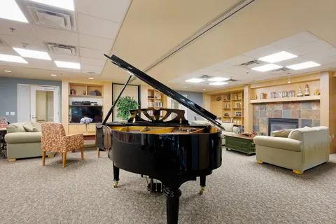 Common room with a grand piano, sofas and library shelves.