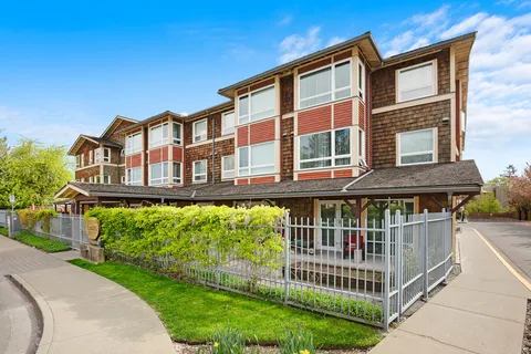 Multi-storey residence with red siding, balconies and planted beds.