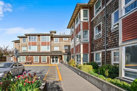Residence entrance drive beside flower beds and parked cars.