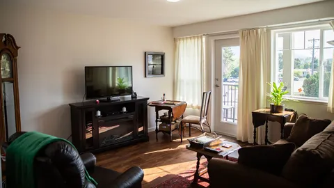 Sitting room with a sofa, armchair, television, small desk and balcony door