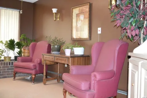 Two pink armchairs beside potted plants and a wooden table