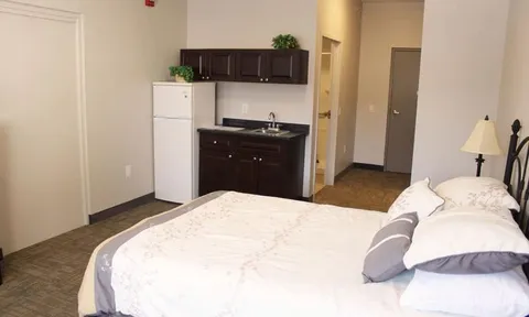 Bedroom with a bed, refrigerator, sink and dark cabinets