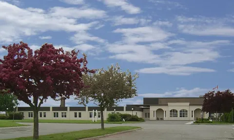 Low building with arched entrance details, trees and a driveway
