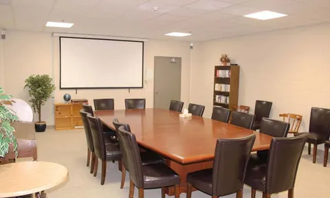Room with a long table, dark chairs, bookshelves and a projection screen