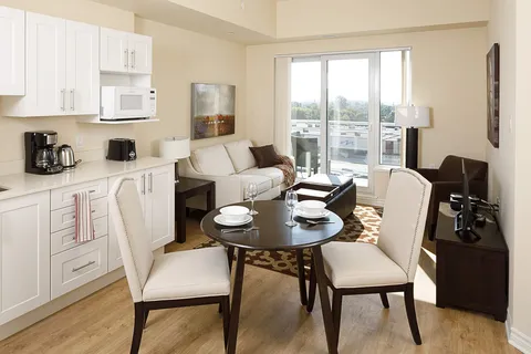 Kitchen and sitting area with white cabinets, a sofa, round table and balcony door