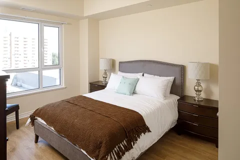 Bedroom with a made bed, bedside cabinets, lamps and a large window