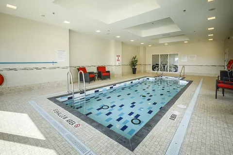 Indoor pool with blue tiles, handrails and red-cushioned chairs