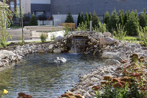 Garden pond with a rock waterfall, shrubs, raised beds and a bench
