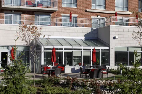 Patio tables and chairs with red umbrellas beside planted beds and residence balconies