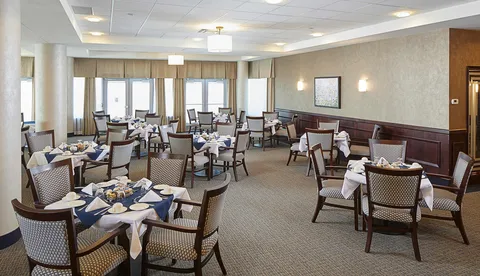 Dining room with set tables, white tablecloths, upholstered chairs and large windows