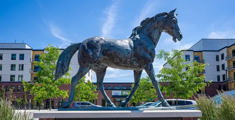 Horse sculpture beside planted garden beds and paths.